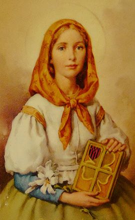 Painting of a girl in traditional Belgian dress with gold headscarf, holding a white lily and a book with shamrock.